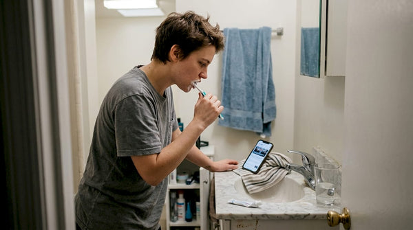 Young adult brushing teeth while checking phone
