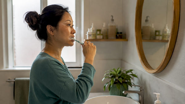 Woman brushing teeth at home bathroom mirror