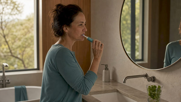 Woman using automatic toothbrush in bathroom