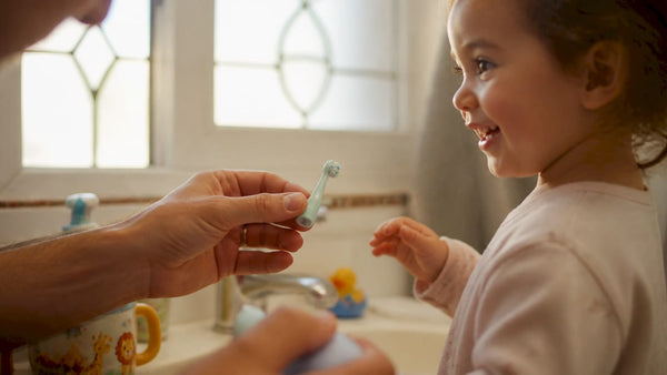 Parent holding child’s electric toothbrush in bathroom