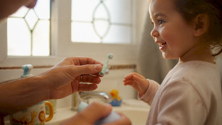Parent holding child’s electric toothbrush in bathroom